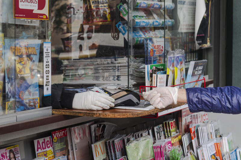 SEVILLE, SPAIN - MARCH 29: A woman wearing latex gloves pays the newspaper with her credit card in a kiosk on March 29, 2020 in Seville, Spain. Spain will forbid all non-essential economic activity until April 9 as Coronavirus quarantine measures continue. The Coronavirus (COVID-19) pandemic has spread to many countries across the world, claiming over 30,000 lives and infecting hundreds of thousands more. (Photo by Niccolo Guasti/Getty Images)