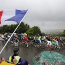 A spectator waves the French flag as the pack climbs in the rain during the fifth stage of the Tour de France cycling race over 189.5 kilometers (117.8 miles) with start in Arras and finish in Amiens, France, Wednesday, July 8, 2015. (AP Photo/Christophe Ena)