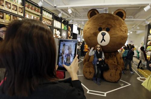 In this March 16, 2015 photo, tourists take their souvenir photos with an outsized Line's character Brown bear at the Line Friends flagship shop in Seoul, South Korea. For smartphone users in Asia where most of Line's 181 million monthly users are located, the characters are as familiar as Hello Kitty or Disney's animated stars. They are not well known in America or Europe but owner Line Corp. hopes to change that. It plans to open 100 stores selling Brown dolls and other cute 
