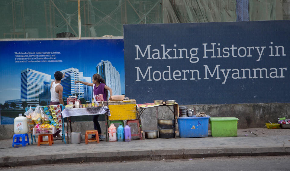 FILE - In this Dec. 3, 2014, file photo, sidewalk restaurant operators catering to construction workers outside a construction site point their fingers at a photograph of the proposed building in Yangon, Myanmar. The military coup in Myanmar is unlikely to do the country’s struggling economy any good at all. The country once considered a promising last frontier has languished as the pandemic added to its challenges. (AP Photo/Gemunu Amarasinghe, File)