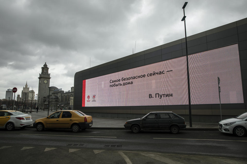 A quote by Russian President Vladimir Putin on a screen reads "The most safe thing now - is to stay at home. V. Putin", with the Foreign Ministry headquarters building, second from left, and Kiyevsky railway station, center, in the background, in Moscow, Russia, Thursday, April 2, 2020. President Vladimir Putin has ordered most Russians to stay off work until the end of the April to curb the spread of the coronavirus. (AP Photo/Pavel Golovkin)