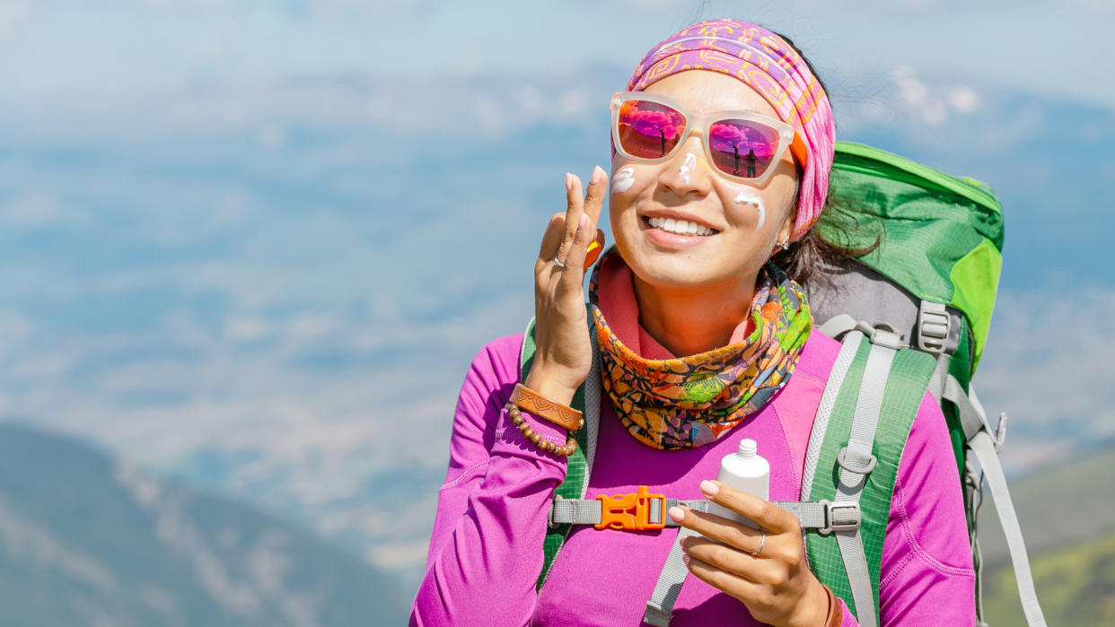  Hiker woman applying sun cream to protect her skin from dangerous uv sun rays high in mountains. 