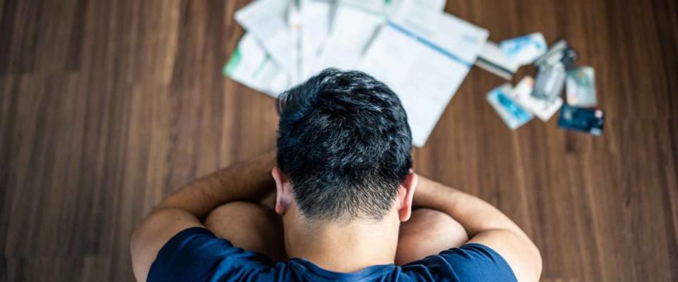 Top view of stressed young man sitting and hugging knees, trying to find money to pay credit card debt