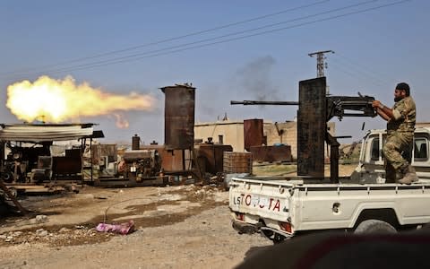 A Turkish-backed Syrian fighter fires during clashes in the border town of Ras al-Ain - Credit: AFP