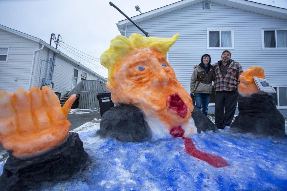 A teenaged boy and his father pose for a photo with a snow sculpture they created on their front lawn in St. John’s, NL, on Jan. 20, 2021, depicting Trump descending into the water. THE CANADIAN PRESS/Paul Daly