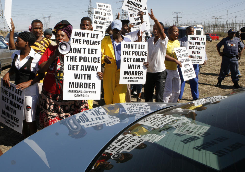 A group of protestors holds placards as a large crowd followed retired judge Ian Farlam and his team as they inspected the area where the bodies of mine workers were found after the shootings at Lonmin's platinum mine in Marikana near Rustenburg, South Africa, Monday, Oct. 1, 2012. Farlam, is conducting an inquiry into the shootings at the platinum mine. (AP Photo/Themba Hadebe)