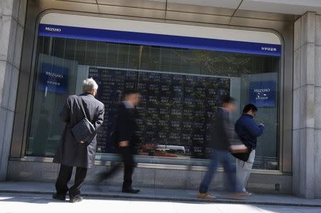 A man (L) looks at a stock quotation board outside a brokerage in Tokyo April 14, 2014. REUTERS/Issei Kato