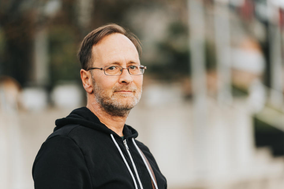 Middle-aged man wearing glasses and black sweatshirt with serious expression