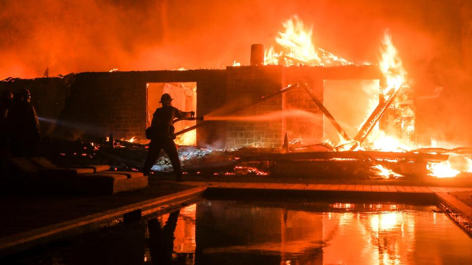 In this November 2018, file photo, a firefighter battles the Woolsey Fire burning a home in Malibu.