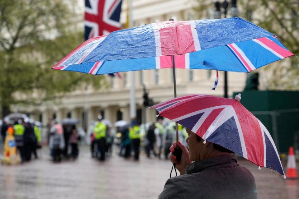 A woman has two British flag umbrellas as she waits in the rain on the Mall, part of the Coronation route in London, Friday, May 5, 2023. King Charles III will be crowned King on Saturday, May, 6. (AP Photo/Alessandra Tarantino)