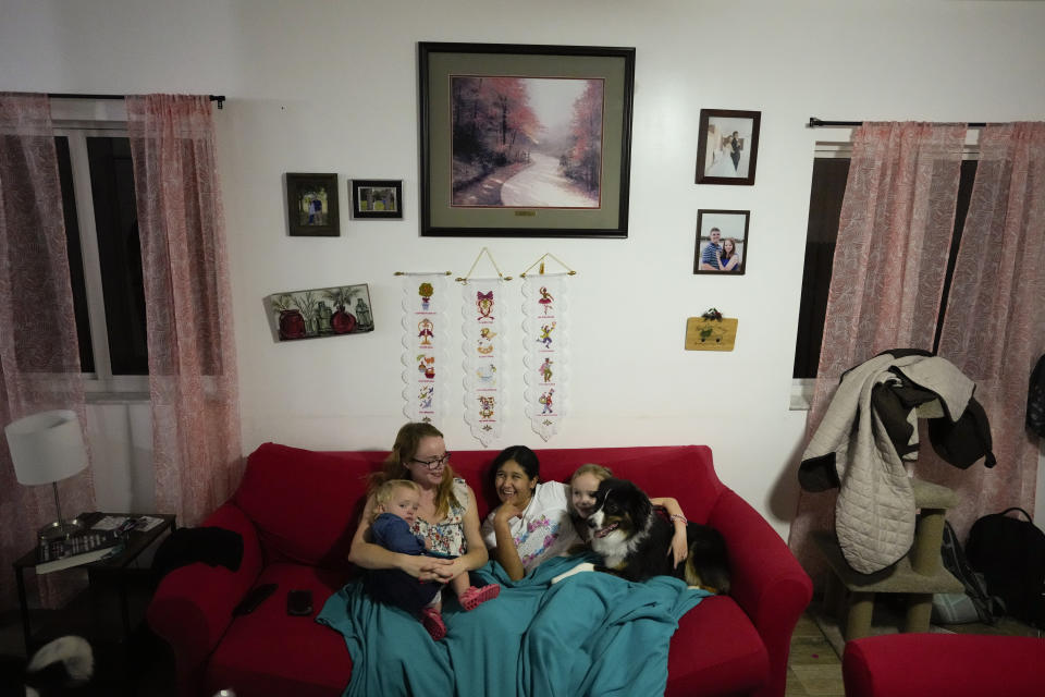 Sol, center, a 14-year-old from Argentina, snuggles up with her foster mother Caroline Hazelton and two of the Hazelton kids, Jessie, left, and Maddie, right, along with Sol's dog Cosmo, in the family's living room in Homestead, Fla., Monday, Dec. 18, 2023. Sol is among tens of thousands of children who have arrived in the United States without a parent during a huge surge in immigrants that's prompting congressional debate to change asylum laws. (AP Photo/Rebecca Blackwell)