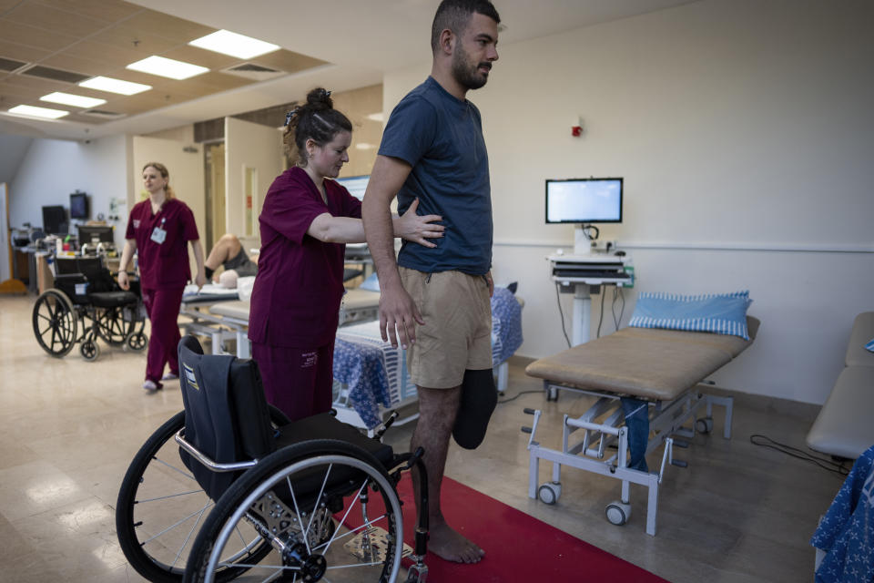 Israeli soldier Jonathan Ben Hamou, 22, wounded in the war with Hamas, practices standing during a physiotherapy session in Sheba Hospital's rehabilitation division in Ramat Gan, Israel, Monday, Dec. 18, 2023. Ben Hamou was wounded in the Gaza Strip when a rocket-propelled grenade struck the bulldozer he was using to help clear the way for other troops and dig trenches. He lost his left leg beneath the knee, and his right leg is covered in shrapnel wounds. (AP Photo/Oded Balilty)