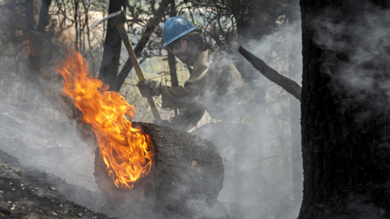 Carson Hot Shots Tyler Freeman works to keep a burning log from rolling down a slope, May 23, 2022, as he and his co-workers work on hot spots from the Calf Canyon/Hermits Peak Fire in the Carson National Forest west of Chacon, N.M. (Eddie Moore/The Albuquerque Journal via AP, File)