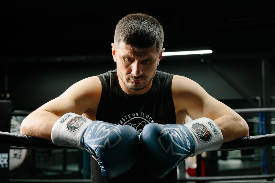 Man wearing boxing gloves leaning over a boxing ring.