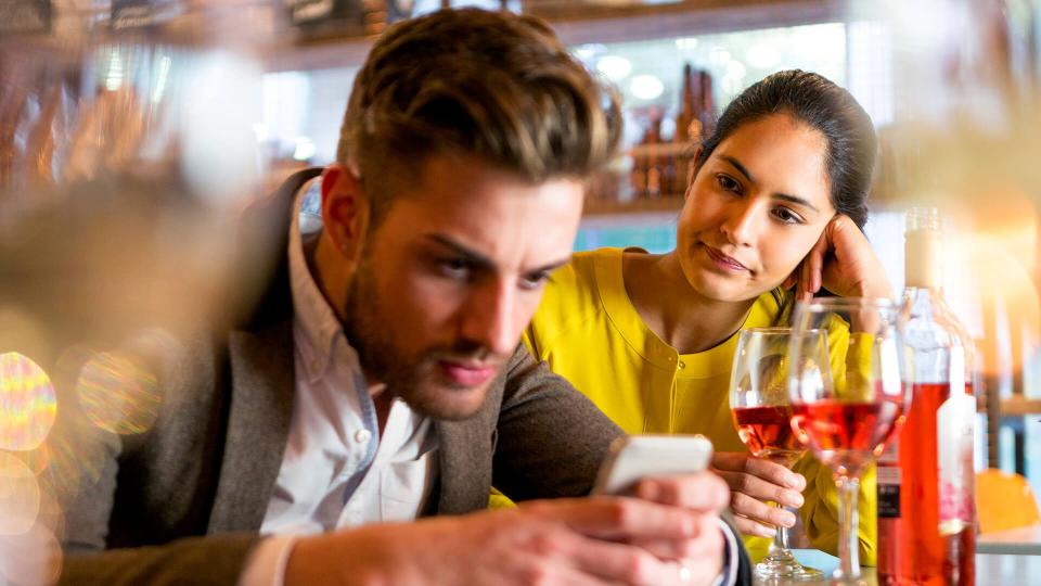 A couple are out having drinks and the woman looks irritated that her partner is on his mobile phone and not paying her any attention.