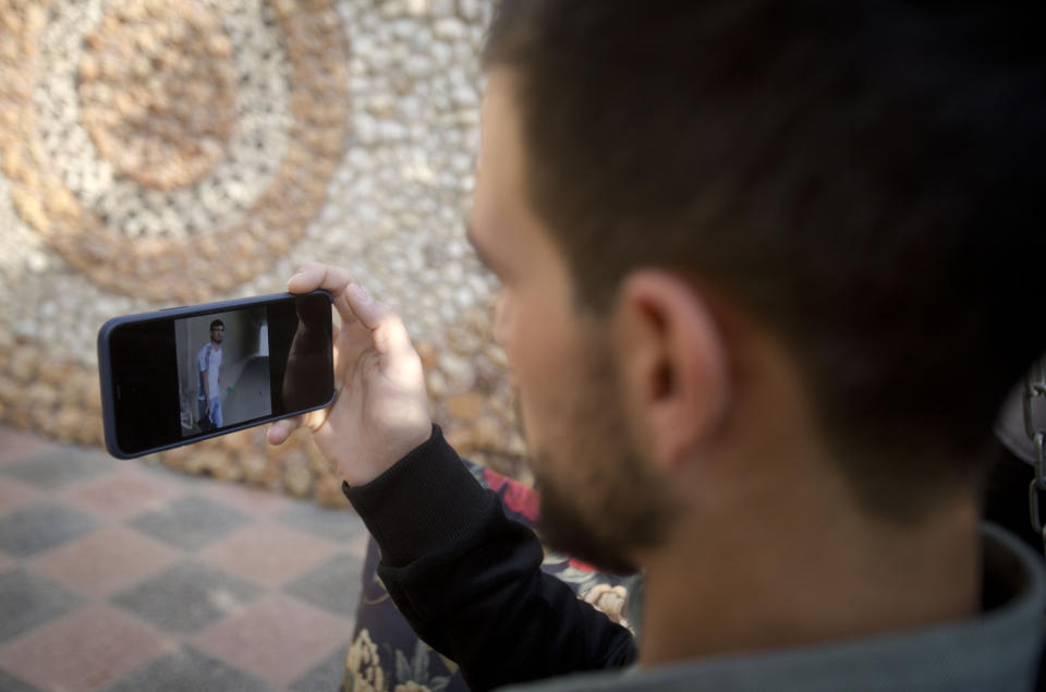 Palestinian Karam Qawasmi looks at a video, which appears to have been taken by a member of the security forces, showing when he was shot in the back by Israeli forces in an incident last year, in the garden of his house, in the West Bank city of Hebron, Sunday, Nov. 10, 2019. Qawasmi said that the footage shows just a small part of what was a horrifying day for him. In his first interview since the video emerged last week, Qawasmi said he was run over by a military jeep, then beaten for several hours before troops released him, only to shoot him in the back with a painful sponge-tipped bullet as he walked away. (AP Photo/Majdi Mohammed)