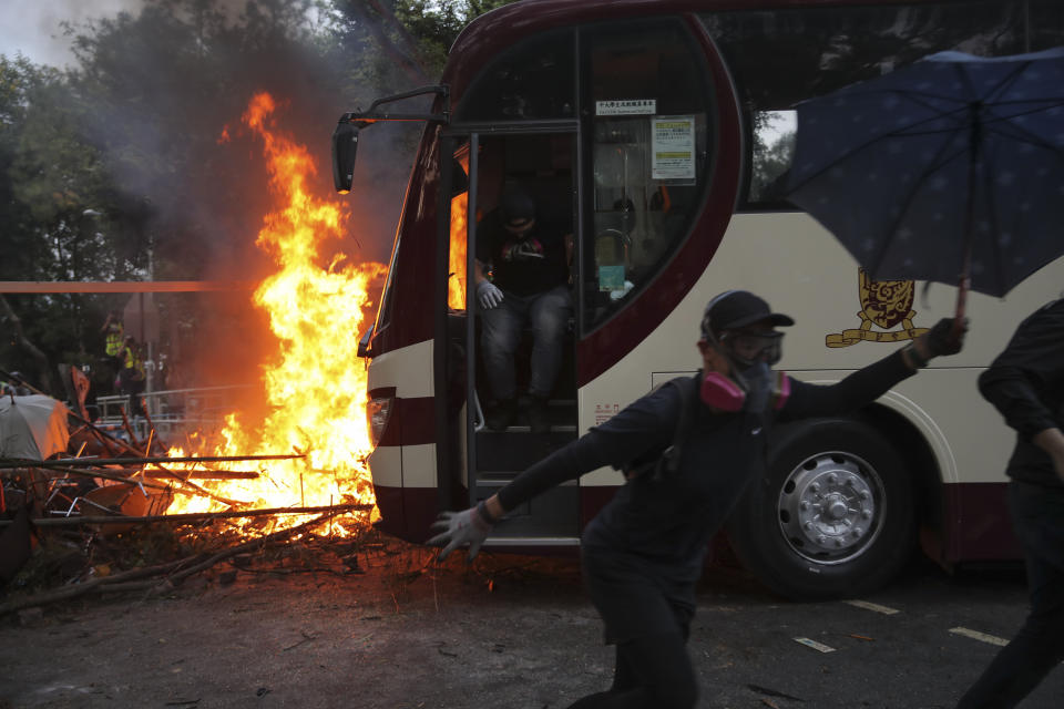 Students run past fire set near a bus during a face-off with riot police at the Chinese University in Hong Kong, Tuesday, Nov. 12, 2019. Police fired tear gas at protesters who littered streets with bricks and disrupted morning commutes and lunch breaks Tuesday after an especially violent day in Hong Kong's five months of anti-government demonstrations. (AP Photo/Kin Cheung)