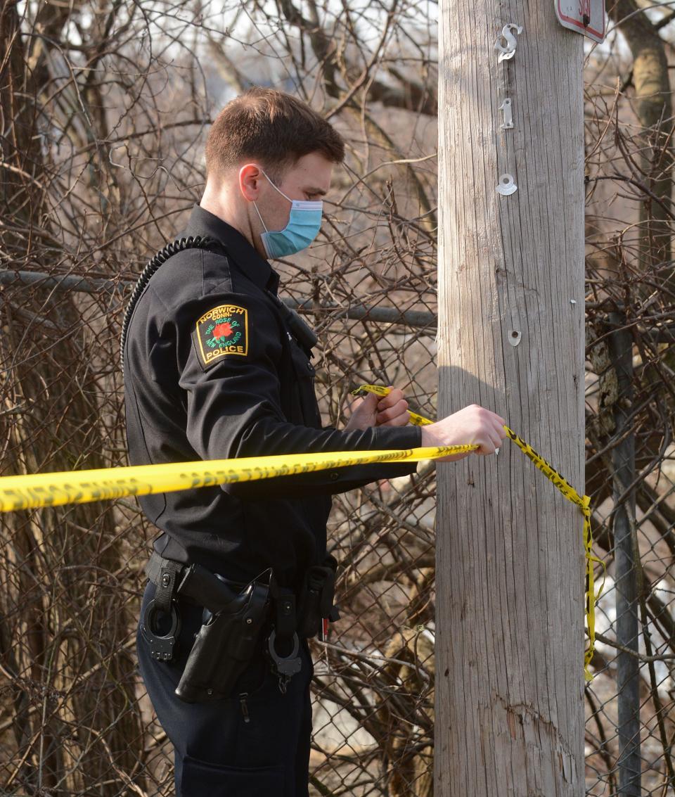 Norwich Police officer John Santos, Jr. ties a crime tape on a pole outside 40 School Street in downtown Norwich Monday after a fatal shooting that happened Sunday night.