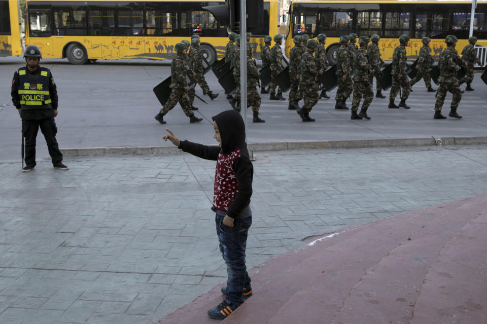 FILE - In this Nov. 5, 2017, file photo, a child reacts as security personnel march by in a show of force in Kashgar in western China's Xinjiang region. A Chinese Communist Party official signaled Monday, Dec. 21, 2020 that there would likely be no let-up in its crackdown in the Xinjiang region, but said the government's focus is shifting more to addressing the roots of extremism. (AP Photo/Ng Han Guan, File)