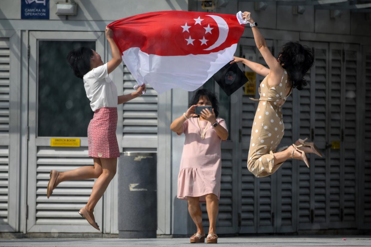 TOPSHOT - Women holding the Singapore national flag pose for a photograph at the Merlion Park to mark the 55th National Day celebrations in Singapore on August 9, 2020. (Photo by Roslan RAHMAN / AFP) (Photo by ROSLAN RAHMAN/AFP via Getty Images)