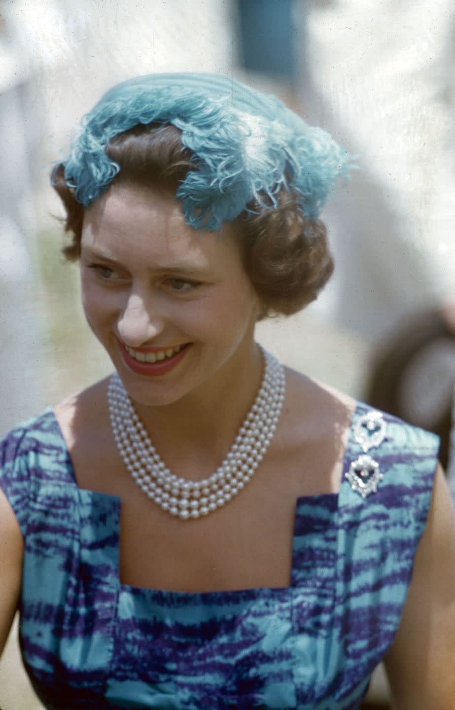 <p>Princess Margaret sports a feathered blue hat, pearls, and patterned dress during her royal tour of East Africa in 1956.</p>