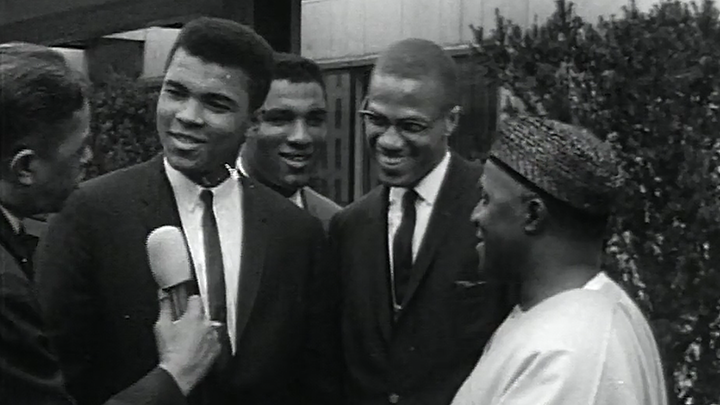 MALCOM X & MUHAMMAD ALI (L to R) MUHAMMAD ALI talking to a reporter smiling