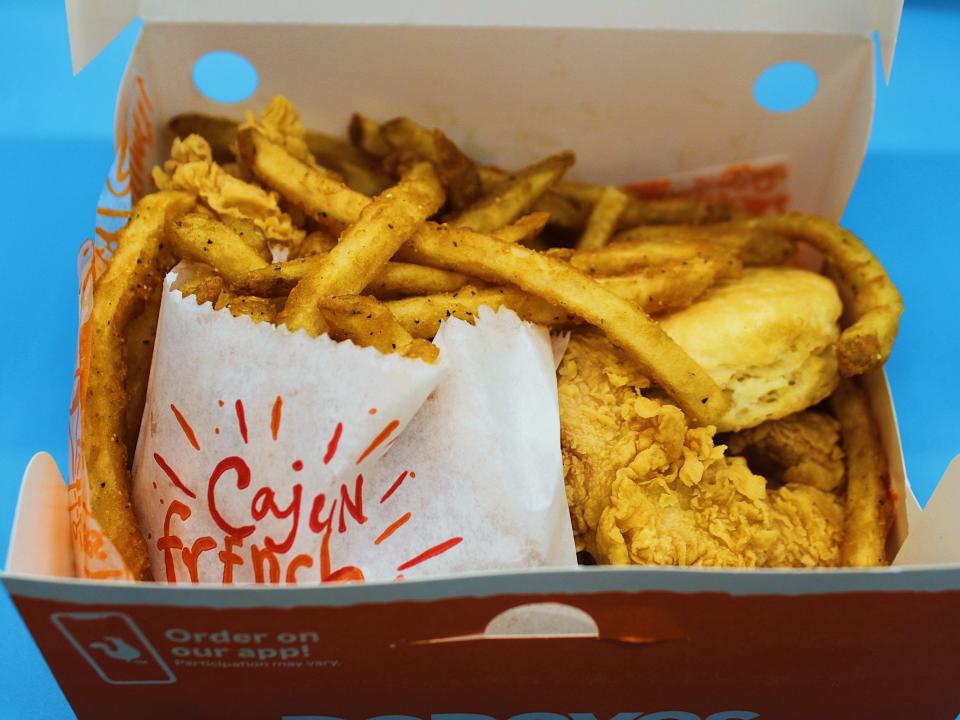 popeyes box of cajun fries chicken tenders biscuit on blue background