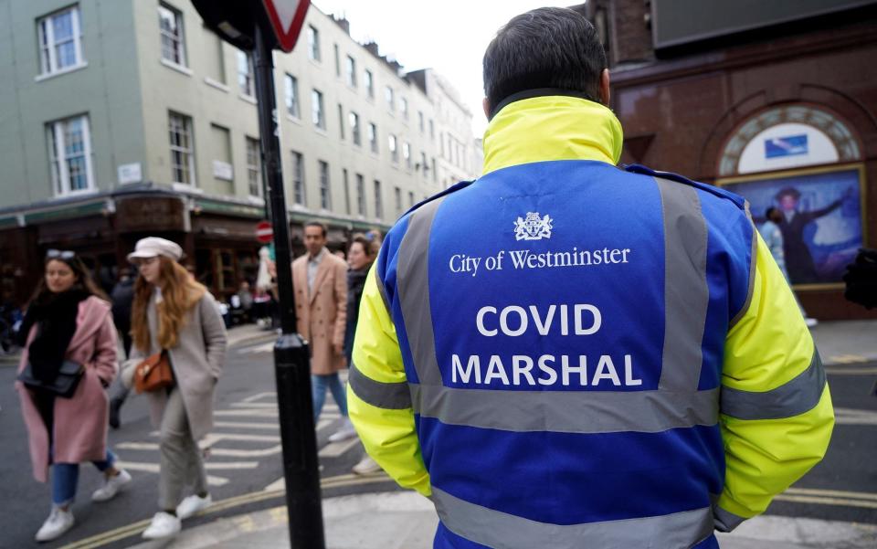 A 'Covid Marshall' from Westminster City Council stands on duty as people drink at re-opened bars in the Soho area of London - NIKLAS HALLE'N/AFP via Getty Images