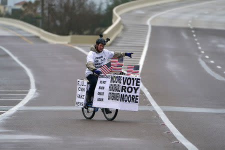 A man rides his bike with signs of support for Alabama Republican senatorial candidate Roy Moore around a venue that will host U.S. President Donald Trump later in the day in Pensacola, Florida, U.S., December 8, 2017. REUTERS/Carlo Allegri