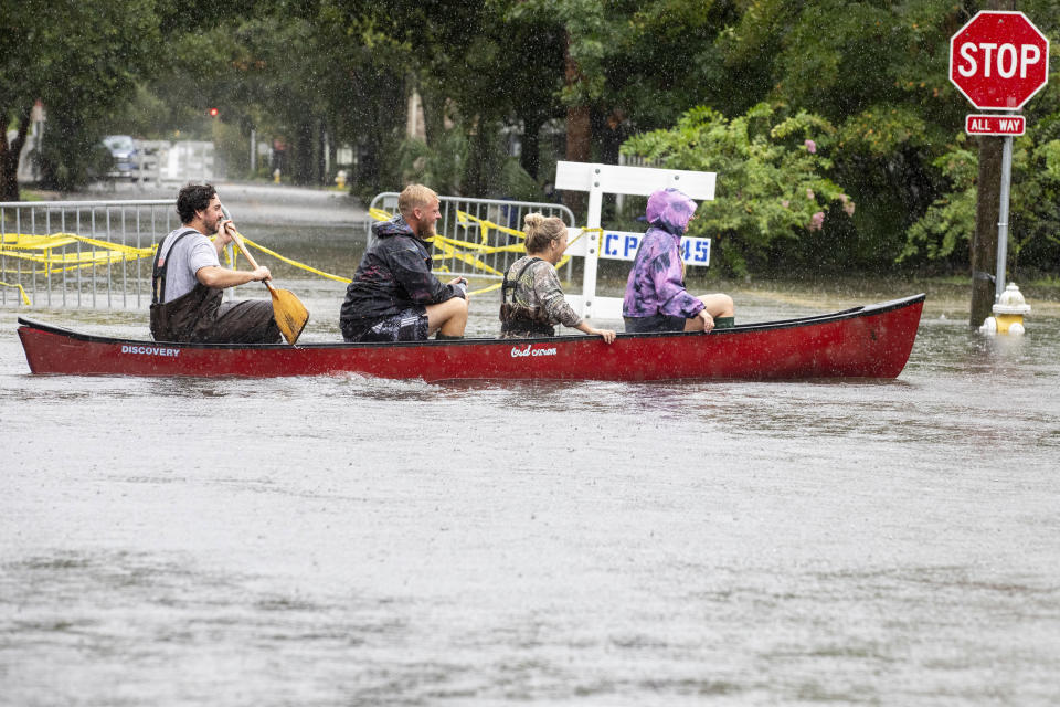 Four people sit in a canoe next to a partially submerged fire hydrant and stop sign.