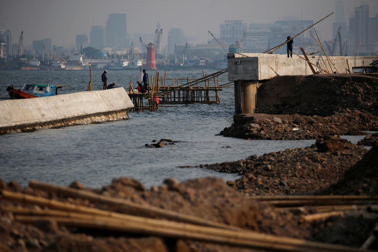 A worker carries a bamboo stick at a crumbled sea wall in an area affected by land subsidence and rising sea levels, in northern coast of Jakarta, Indonesia, December 9, 2019. Picture taken December 9, 2019. REUTERS/Willy Kurniawan