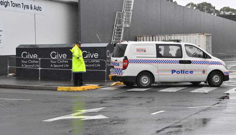 A Queensland police officer in a high-visibility jacket on next to the charity bin, with a van parked nearby.
