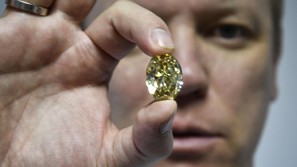 Russian Alrosa Diamond Deputy Director for sales Yevgeny Tsybukov shows a coloured, fancy brownish greenish yellow oval diamond, 50,21 carats, at Alrosa Diamond Cutting Division in Moscow on July 3, 2019. - Russian Alrosa gets its diamonds in the permafrost abyssal holes dug with explosives in the permanently frozen ground of Yakutia, an isolated region in East Siberia, the home to the huge diamond deposits that ensure Russia's supremacy in world production. (Photo by Alexander NEMENOV / AFP)        (Photo credit should read ALEXANDER NEMENOV/AFP via Getty Images)