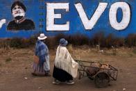 Women walk past a wall with a graffiti depicting former Bolivian President Evo Morales, before general elections in La Paz