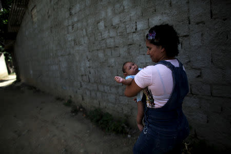Jackeline Vieira de Souza, 26, holds her four-month-old son Daniel who was born with microcephaly, as they walk toward their house in Olinda, near Recife, Brazil, February 11, 2016. REUTERS/Nacho Doce/File Photo
