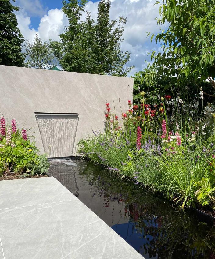 <p> This striking set-up is part of a sleek outdoor living, relaxing, and entertaining space designed by Consilium Hortus.&#xA0; </p> <p> The minimal hardscaping strikes a beautiful contrast against the organic forms of hot-hued planting. And note how the rill, dyed an inky black, adds an additional sense of drama when juxtaposed against the pale paving and feature wall.&#xA0; </p> <p> Not only is it a sophisticated focal point, it&apos;s an integral feature of the plot&apos;s layout: what&apos;s not shown in this image is the way it extends to cleverly separate a covered seating area from a dining zone. </p>