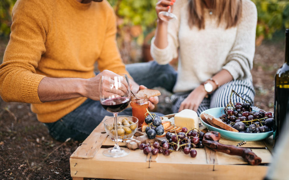 Young happy couple at picnic after grapes harvest, eating and tasting wine