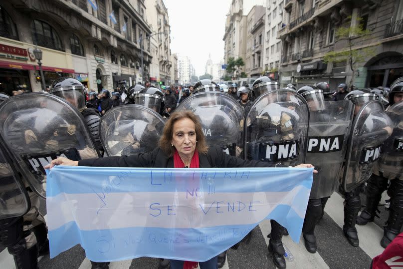 An anti-government protester holds an Argentine flag by police near Congress where lawmakers debate a reform bill promoted by Argentine President Javier Milei in Buenos Aires.