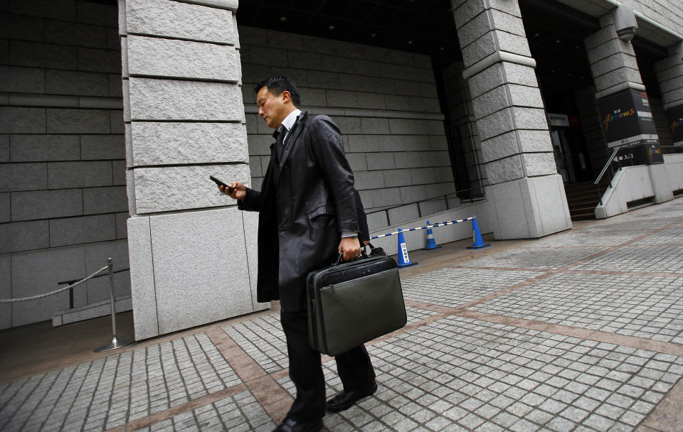 In this Thursday, Feb. 13, 2014 photo, a man checks his mobile phone as he walks in the business district in Tokyo. Over the past two decades Japan’s system of salaried jobs with full benefits has crumbled companies struggled to stay afloat in cut-throat global markets, , shifting much of their manufacturing overseas. Steady jobs in manufacturing and finance that moved abroad or became obsolete were replaced by low-paying service jobs such as clerking in convenience stores and delivery work, especially for workers under 40. (AP Photo/Junji Kurokawa)