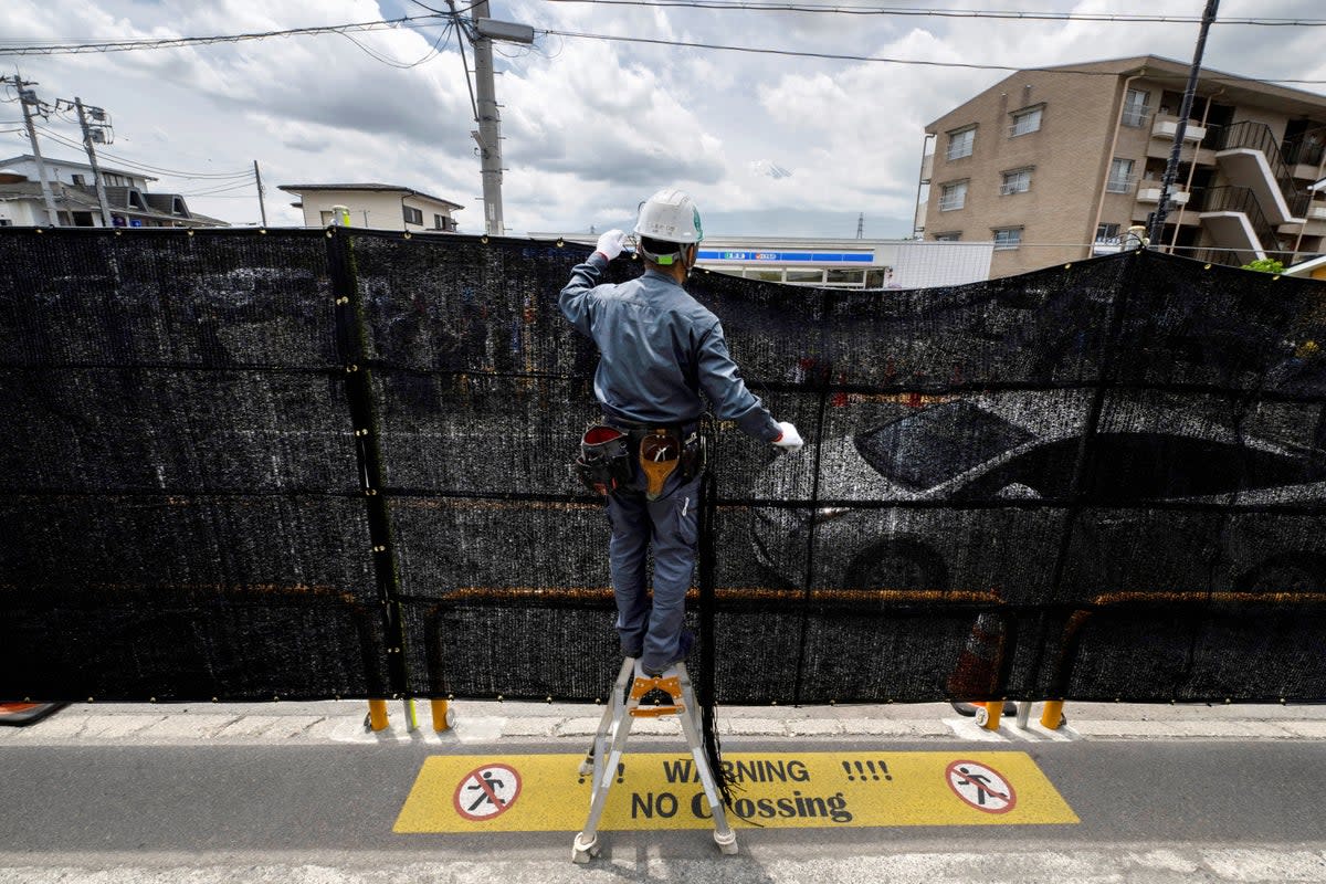 A worker installs a barrier to block the sight of Japan’s Mount Fuji emerging from behind a convenience store to deter badly behaved tourists, in the town of Fujikawaguchiko, Yamanashi prefecture (AFP via Getty Images)