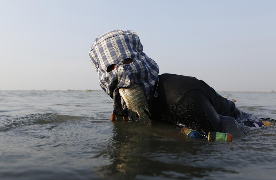 RNPS - PICTURES OF THE YEAR 2013 - Fisherman Ompong Vargas, 39, wearing a facial mask made of fabric to protect his skin from getting darker, holds a fish in his mouth as he uses his hands to search for a net at Laguna de Bay in Taguig City, Metro Manila May 24, 2013. During the dry season, fishermen earn $2-$7 (70-300 pesos) per day. Men's beauty treatments are popular in the Philippines, part of a thriving market for male cosmetics in the Asia Pacific region. Some Filipino men go to great lengths to preserve their faces, from those who visit clinics to receive skin treatments, to fishermen who wear fabric masks while working to protect their skin from the sun. REUTERS/Cheryl Ravelo (PHILIPPINES - Tags: SOCIETY HEALTH TPX ANIMALS)