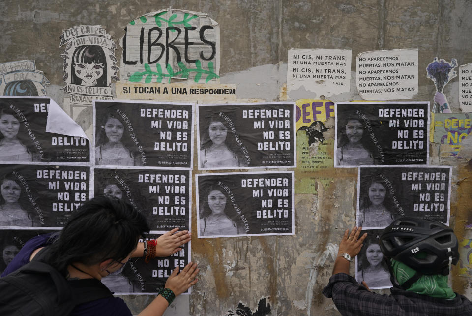 Activistas pegan volantes con la fotografía de Roxana Ruiz con la frase "Defender mi vida no es delito" en un muro cerca del edificio de la corte donde la mujer de 22 años enfrenta una audiencia en que es acusada de homicidio con exceso de legítima defensa en Chimalhuacán, Estado de México, México, el lunes 18 de abril de 2022. Ruiz dijo haber matado a un hombre que la agredió, la violó y amenazó con asesinarla en 2021. (AP Foto/Eduardo Verdugo)