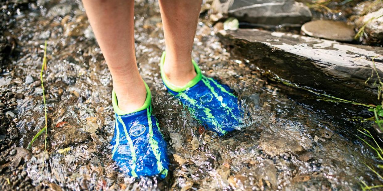 kid standing in rocky river wearing blue and green water shoes