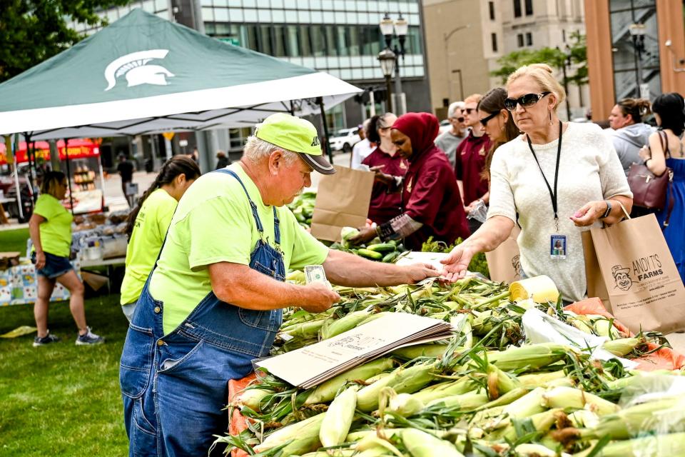 Andy Todosciuk, left, gives a customer change at his booth, Andy T's Farms, on Tuesday, July 18, 2023, during the Farmers Market at the Capitol in downtown Lansing.