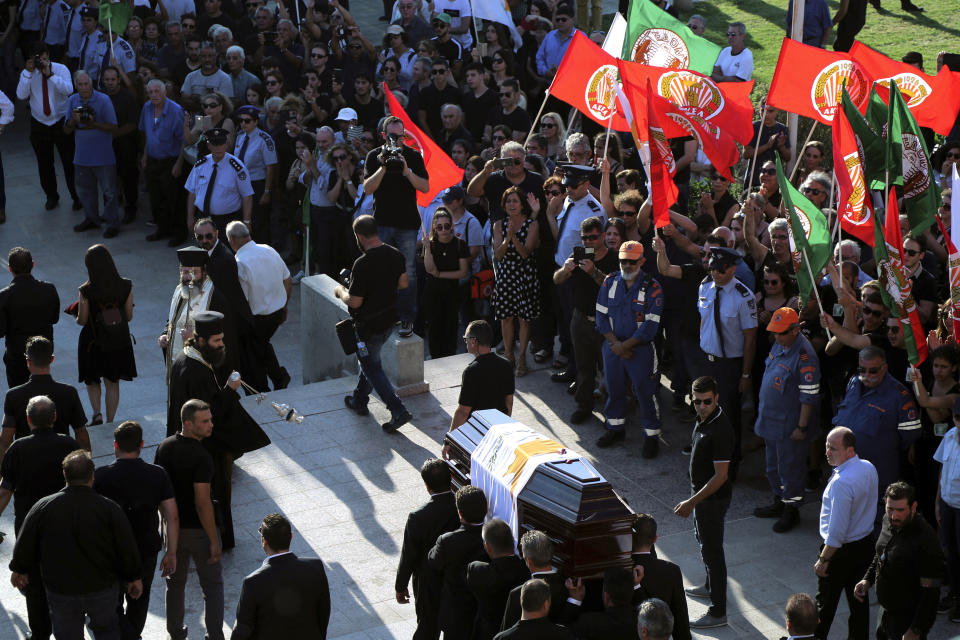 Pallbearers carry the coffin of the former Cyprus' President Dimitris Christofias, as people wave flags of communist party (AKEL) during his state funeral at the Orthodox Christian Church of the Lord's Wisdom in capital Nicosia, Cyprus, Tuesday, June 25, 2019. European communist and left-wing party heads and leaders from ethnically split Cyprus' breakaway Turkish Cypriot community were among those attending a funeral service for the country's former president Christofias. (AP Photo/Petros Karadjias)