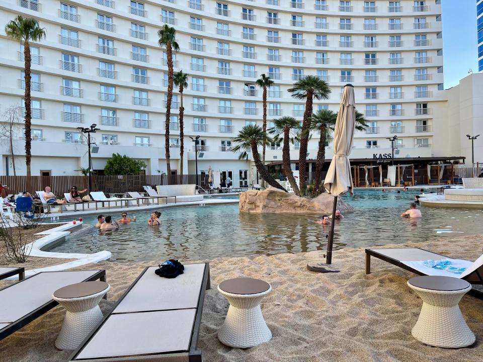 Pools at Virgin hotel surrounded by sand with palm trees and view of tall hotel buidling behind it