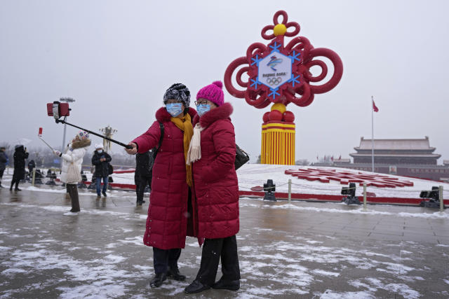 FILE - Women wearing face masks printed with a slogan for the Beijing Winter Olympics Games take a selfie with a decoration for the Winter Olympics Games in Tiananmen Square in Beijing on Jan. 20, 2022. The omicron variant is making its latest appearance, and Beijing is locking down some residential communities as the country anxiously awaits the start of the Winter Olympics on Feb. 4. (AP Photo/Andy Wong, File)