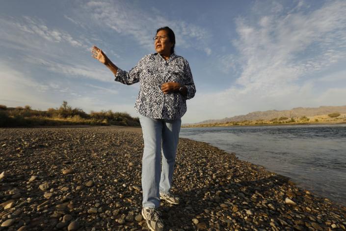 A woman gestures while speaking and walking along a river
