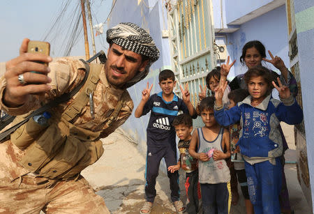 A Kurdish Peshmerga fighter takes a selfie with children after recapturing the Fadiliya village from Islamic state militants, in Nawaran North of Mosul, Iraq, October 27, 2016. REUTERS/Air Jalal