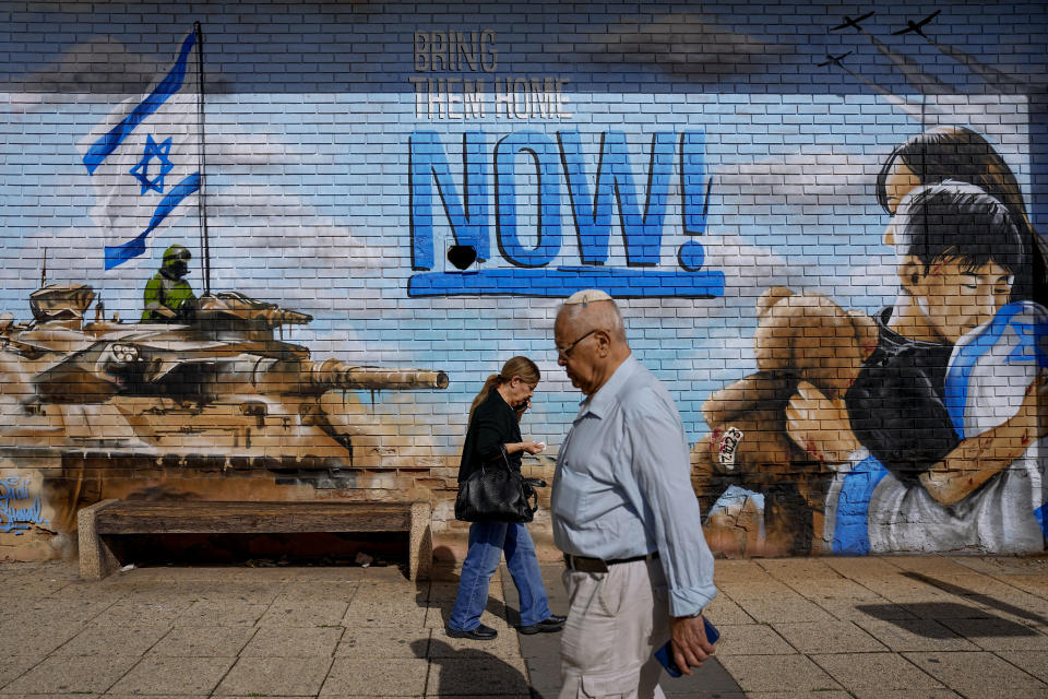 People walk past graffiti calling for the return of the hostages kidnapped during the Oct. 7 Hamas cross-border attack in Israel, in Kfar Saba, Israel, Thursday, Nov. 23, 2023. (AP Photo/Ariel Schalit)